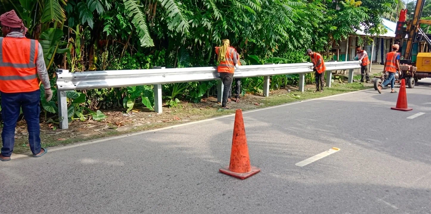 Workers beside a roadside rail and traffic cones